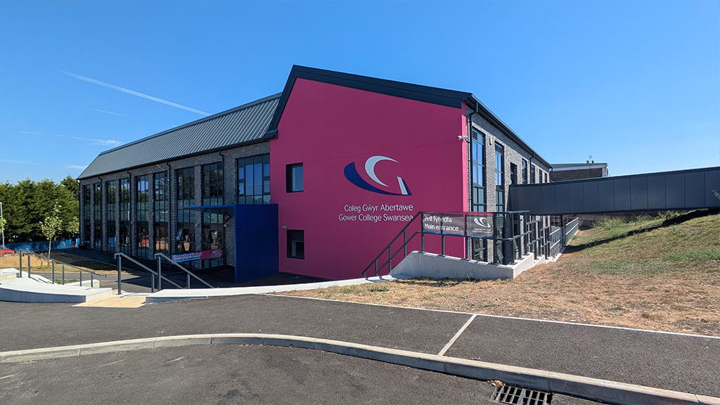 The outside of the new block featuring a pink wall with the Gower College Swansea logo and main entrance