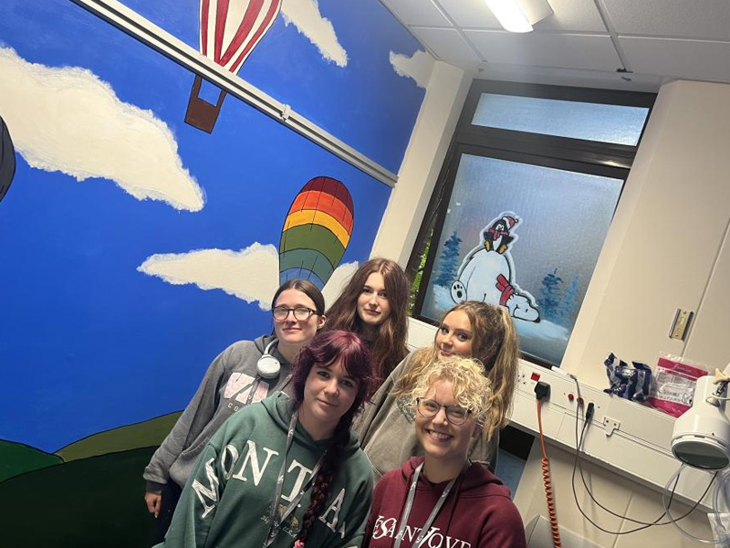 Group of art students next to wall in hospital that they have painted