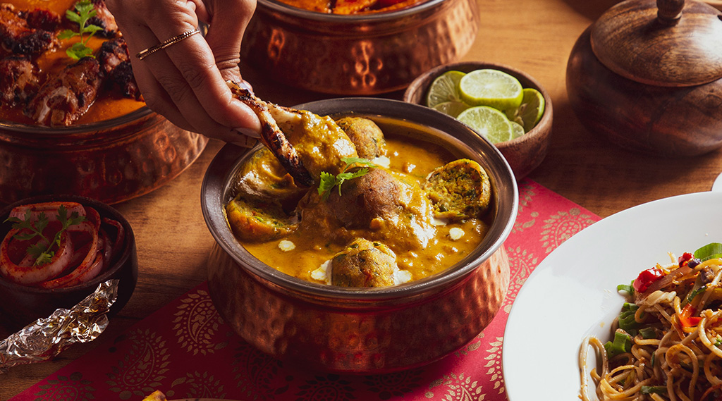 A spread of Indian food with a hand dipping naan in curry