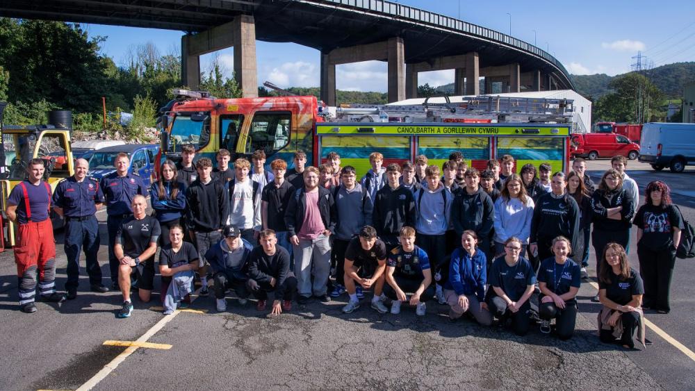 Large group of people standing next to fire engine, bridge in background and blue sky