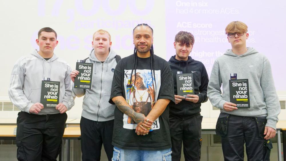 Man in black t-shirt, standing with male students holding books