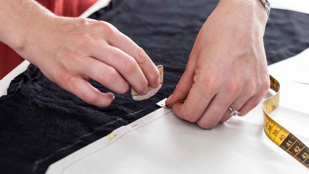 Person marks cloth with chalk as they hold a measuring tape
