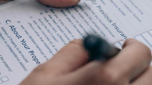 Close up of a hand holding a pen and filling in a paper form