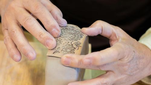 Person using stencil to make shapes on clay pot