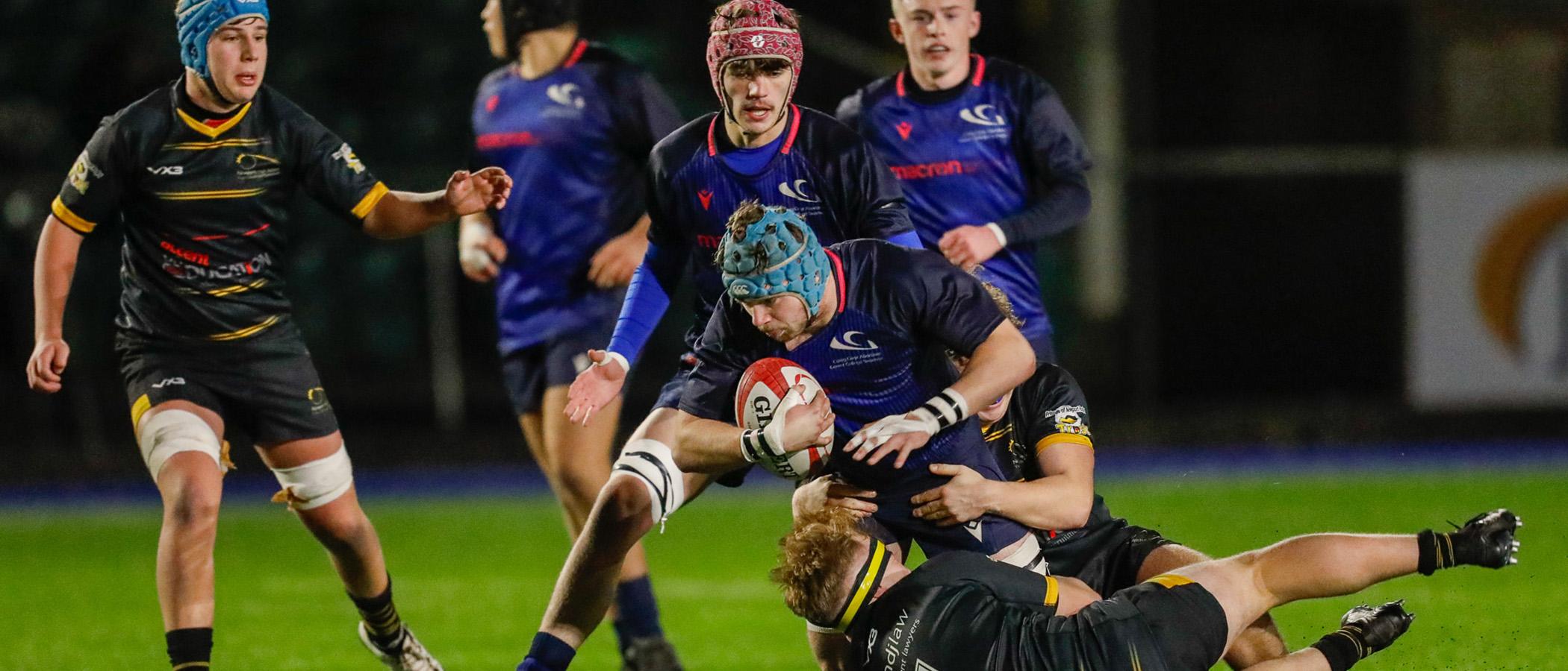 Student rugby players on the pitch mid-tackle