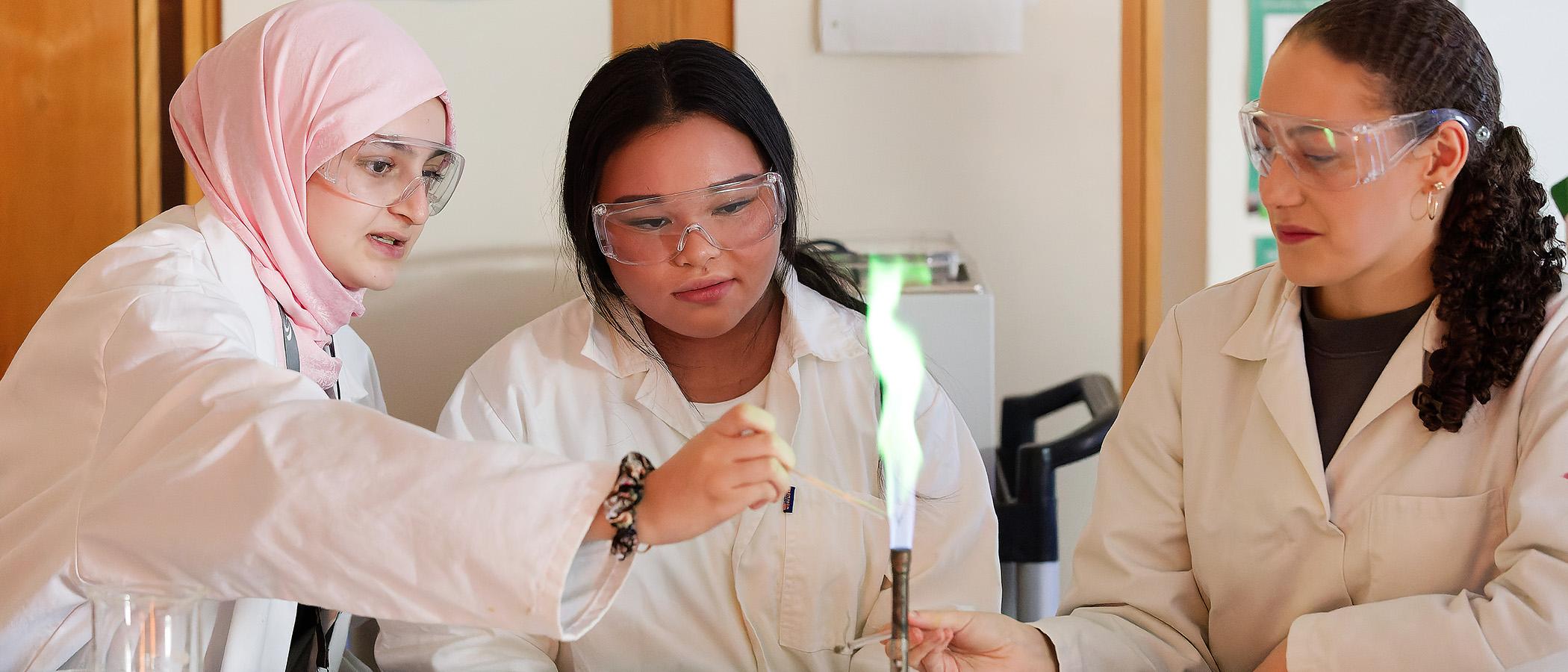 Three students in lab coats with bunsen burner