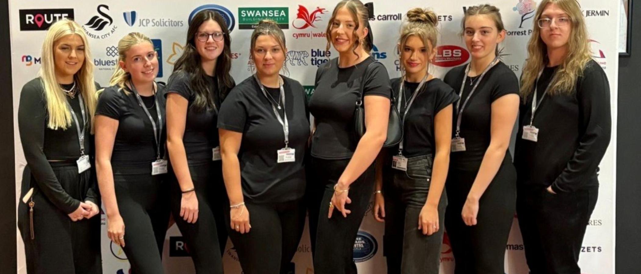 Group of eight young people at event, wearing black and smiling