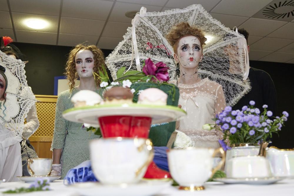 Models in white makeup, with tea cups and cakes