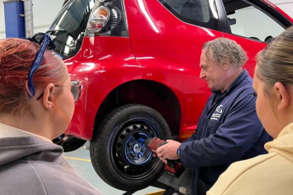Two girls being shown how to remove a wheel