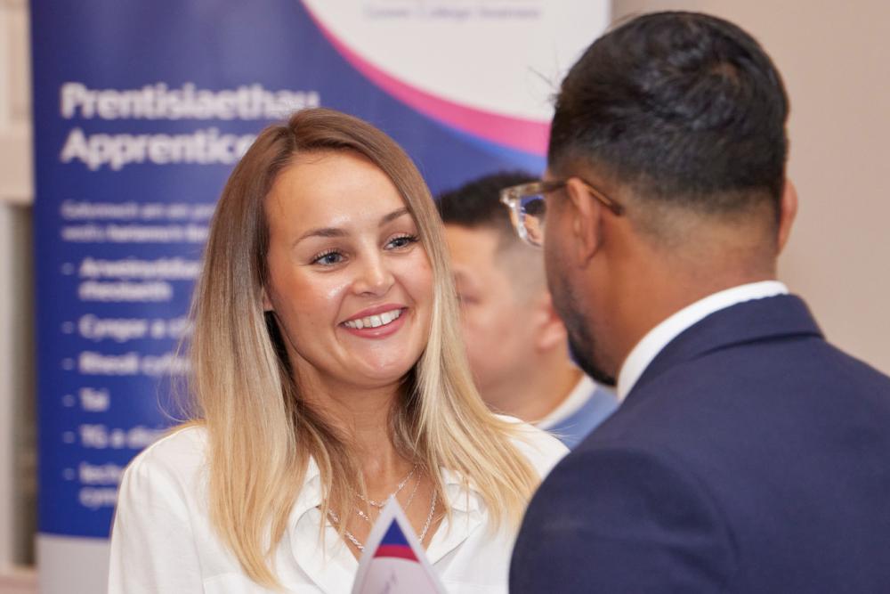 Two people chatting with a Gower College Swansea apprenticeship banner behind them